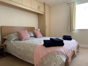A bedroom with a bed, a nightstand, a wooden wardrobe, and a window with curtains.