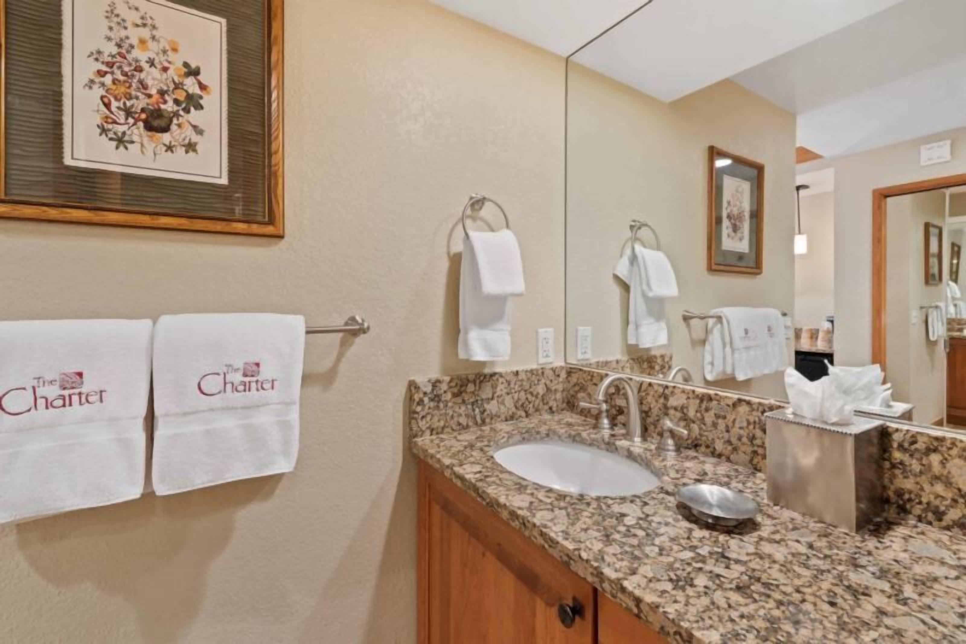 Une salle de bain avec un lavabo doté d’un plan de travail en granit, un miroir et deux œuvres d’art florales encadrées accrochées au mur.