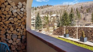Un balcon avec une pile de bois de chauffage, un mur de pierre et une vue sur un quartier résidentiel avec des maisons et des arbres.