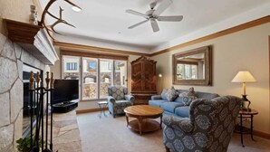 Un salon avec une cheminée, un ventilateur de plafond, un téléviseur, des meubles à motifs et un grand miroir.