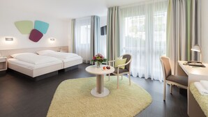 Habitación de hotel con cama, escritorio, silla, televisor y una mesita con un jarrón de flores.