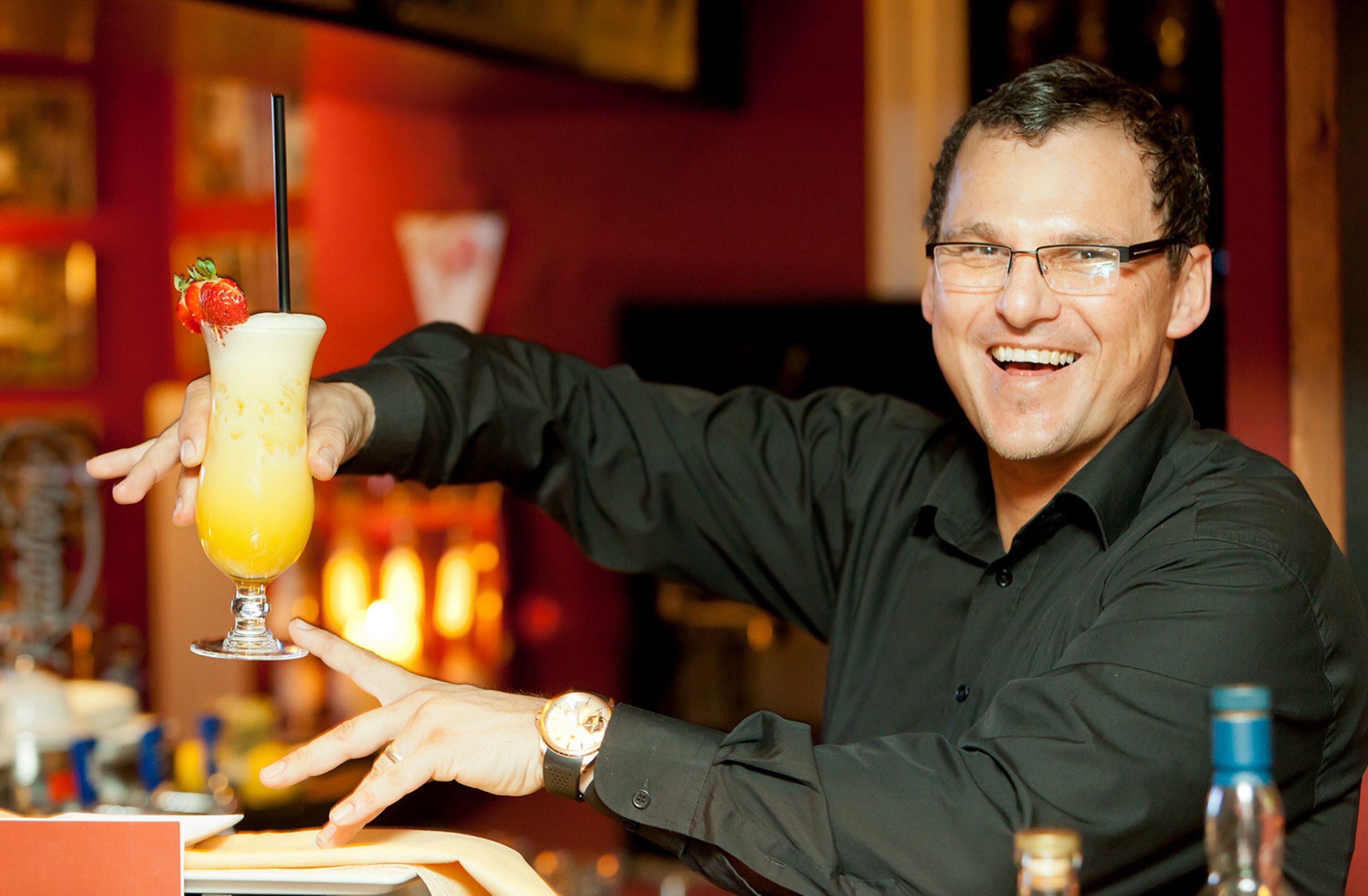 A person holding a cocktail glass with a straw and a strawberry garnish.