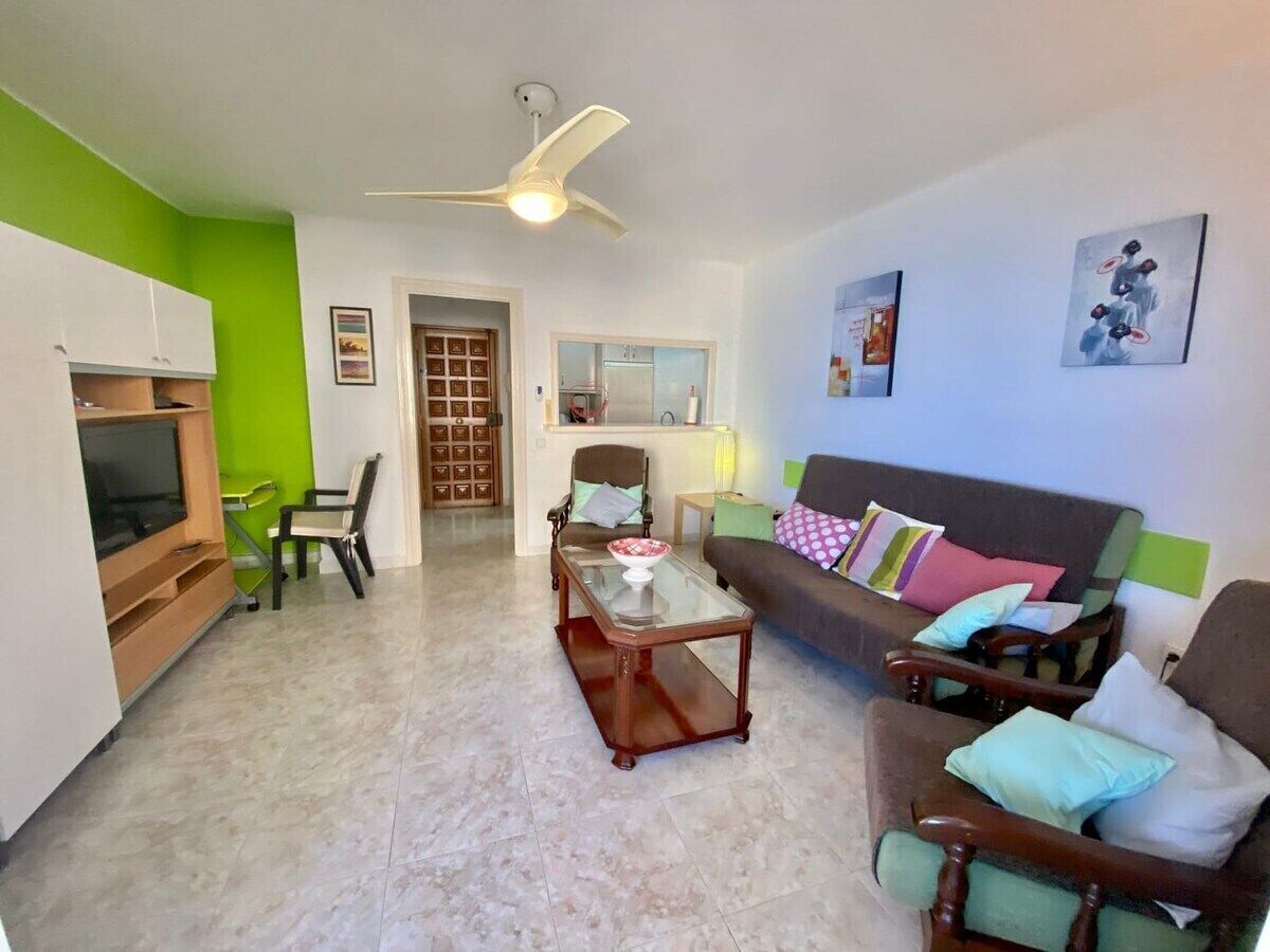 A living room with a sofa, chairs, a coffee table, a TV, and a ceiling fan.