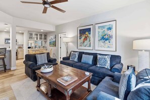 A modern living room with a dark blue sofa set, a wooden coffee table, and two framed abstract paintings.