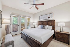 Ein Schlafzimmer mit einem großen Bett, einem Holz-Kopfteil, zwei Nachttischen mit Lampen, einer Bank und einem Deckenventilator.