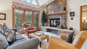 Una sala de estar acogedora con chimenea de piedra, asientos cómodos y grandes ventanales con vistas al exterior.