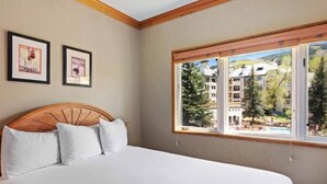 Ein Schlafzimmer mit einem Holz-Kopfteil, weißer Bettwäsche und einem großen Fenster mit Blick auf Gebäude und Bäume.