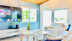 Una sala de estar moderna con un televisor de pantalla plana mostrando opciones de películas, un sofá blanco y una mesa de centro de vidrio.
