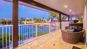 Un balcón con vista a una piscina y palmeras, un sofá de mimbre y una bandera estadounidense.