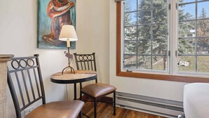 Una habitación con suelo de madera, una mesa redonda con dos sillas, una lámpara y un cuadro en la pared.