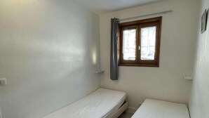 A small, single-room with two beds, a window with curtains, and a light switch on the wall. - 300m from resort center, 1st floor, balcony, parking, tv, ski locker, 28m², Praz sur Arly (Praz-sur-Arly)