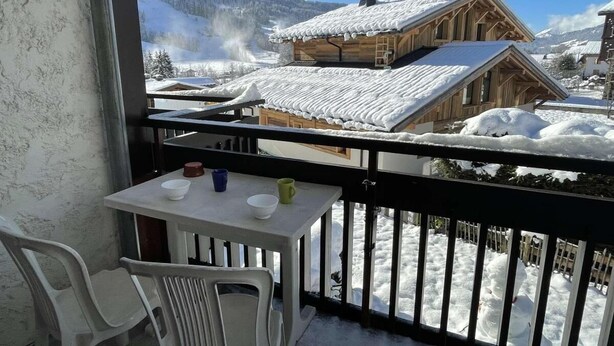 A balcony with a table and chairs, overlooking a snowy village with wooden houses. - 300m from resort center, 1st floor, balcony, parking, tv, ski locker, 28m², Praz sur Arly (Praz-sur-Arly)