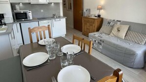 A modern kitchen with white cabinets, a microwave, and a dining table set for four. - 300m from resort center, 1st floor, balcony, parking, tv, ski locker, 28m², Praz sur Arly (Praz-sur-Arly)