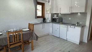 A compact kitchen with white cabinets, a microwave, a coffee maker, and a sink. There is a dining table with chairs and a window with curtains. - 300m from resort center, 1st floor, balcony, parking, tv, ski locker, 28m², Praz sur Arly (Praz-sur-Arly)
