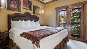 Ein Schlafzimmer mit einem großen Bett, einem Holzkopfstück, einem Nachttisch und einer Tür, die auf einen Balkon mit Blick auf Bäume führt.