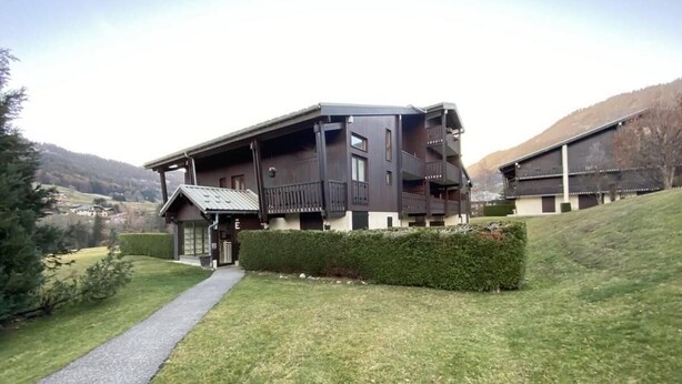 A modern two-story building with a balcony, a paved path leading to the entrance, and a well-maintained lawn.