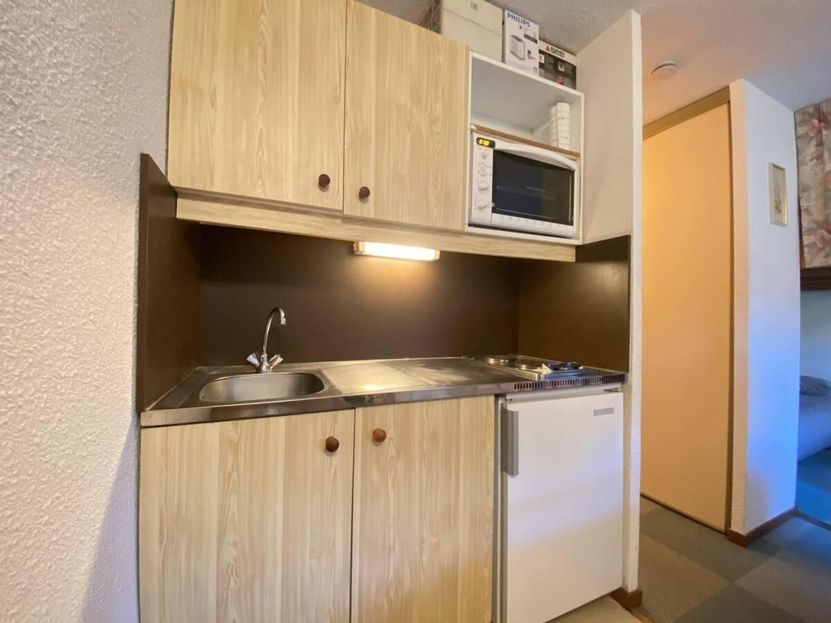 Une cuisine de taille réduite, dotée de meubles en bois, d’un four à micro-ondes, d’un évier et d’un lave-vaisselle.