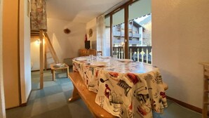 A dining area with a table covered in a tablecloth featuring a cityscape design, a wooden bench, and a view of a balcony with railings.