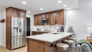 A modern kitchen with wooden cabinets, stainless steel appliances, and a central island with stools. - The Charter at Beaver Creek E130 (Beaver Creek)