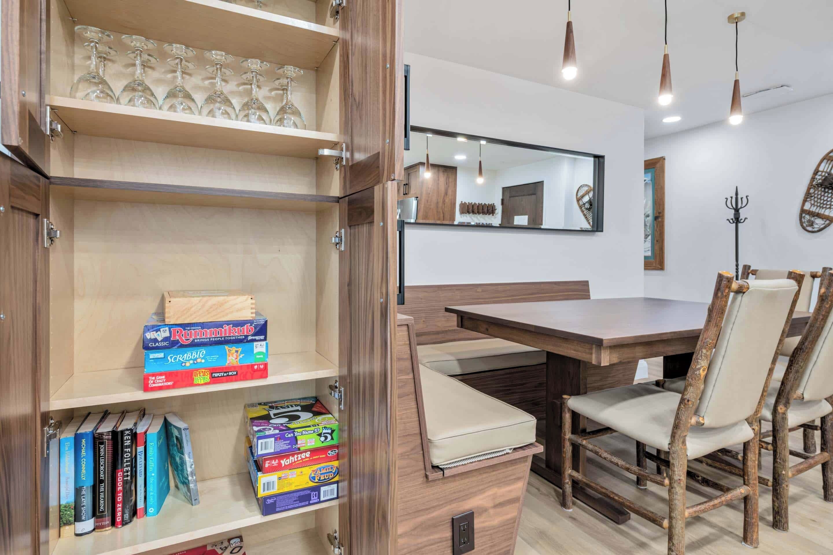 A dining area with a wooden table, a chair, and a bookshelf with games and books.