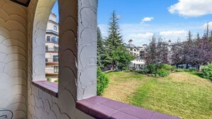 En balkon med udsigt over en velplejet græsplæne, forskellige træer og etageejendomme i baggrunden.