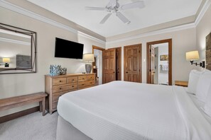 A hotel room with a bed, a television, a desk with a lamp, and wooden doors.