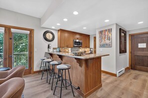 Una cucina moderna con un'isola centrale, sgabelli da bar, pensili in legno e un orologio appeso al muro.