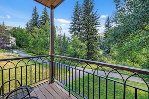 A balcony with a metal railing overlooking a landscaped area with trees and a pathway. - The Charter at Beaver Creek E110 (Beaver Creek)