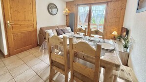 A dining area with a wooden table set for four, a wooden sofa, and a window with curtains.