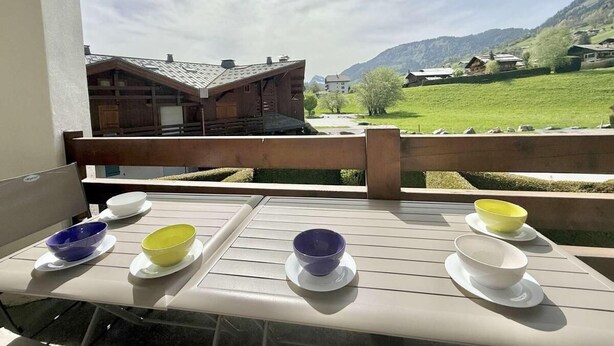 A balcony with a table set for dining, overlooking a mountainous landscape with houses.