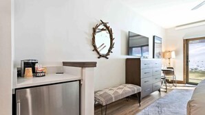 A modern room with a kitchenette, a bench, a dresser, and a large window offering a view.