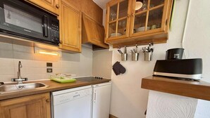 A compact kitchen with wooden cabinets, a microwave, a dishwasher, and a sink. - 300m from resort center, 1st floor, view ski slopes, balcony, parking, tv, ski locker, 35m² (Praz-sur-Arly)