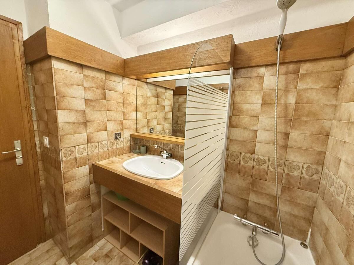 A bathroom with a wooden vanity, a sink, a mirror, and a shower.
