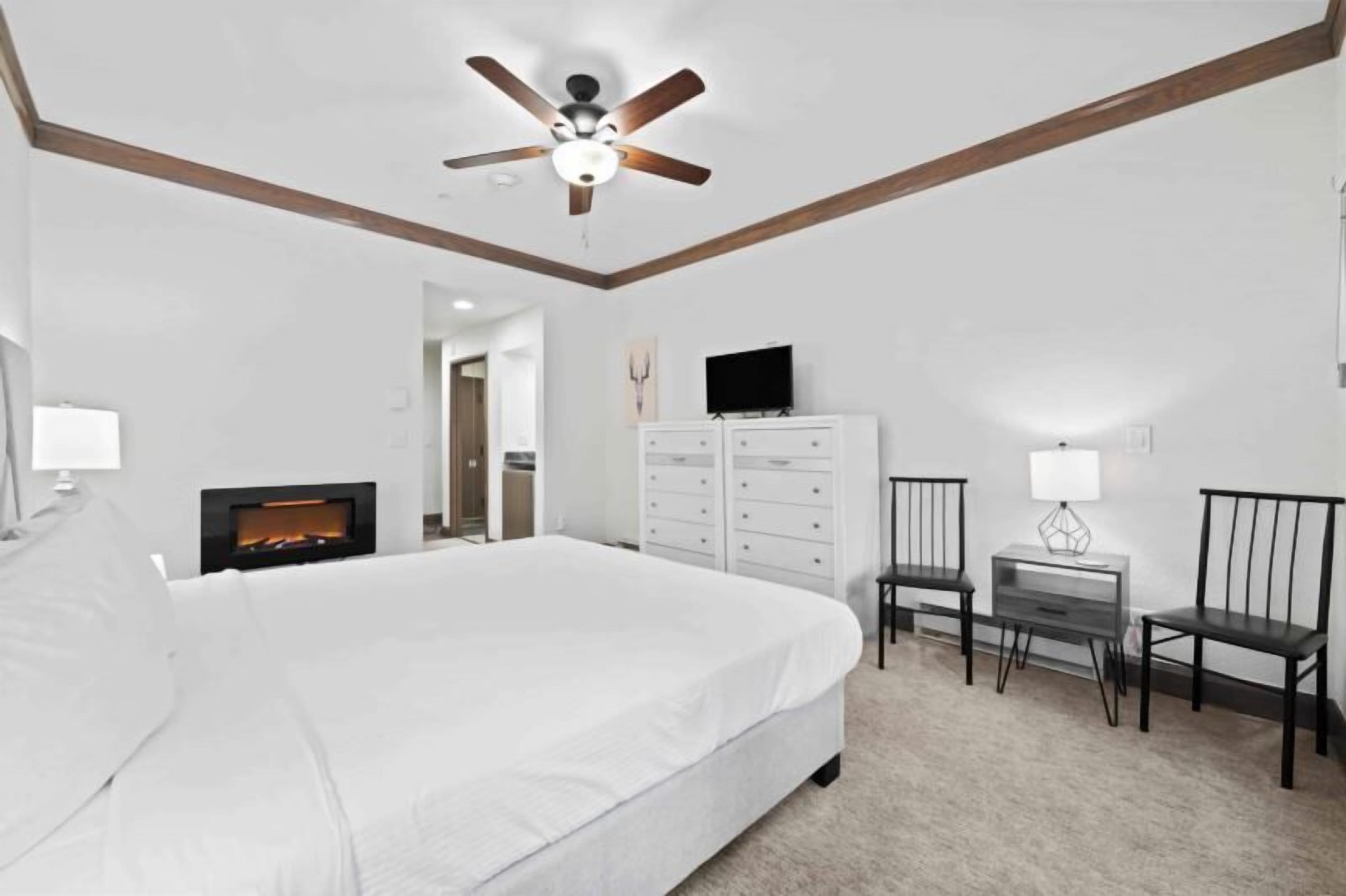 Une chambre à coucher comprenant un lit, un ventilateur de plafond, une télévision, une commode et un bureau avec des chaises.