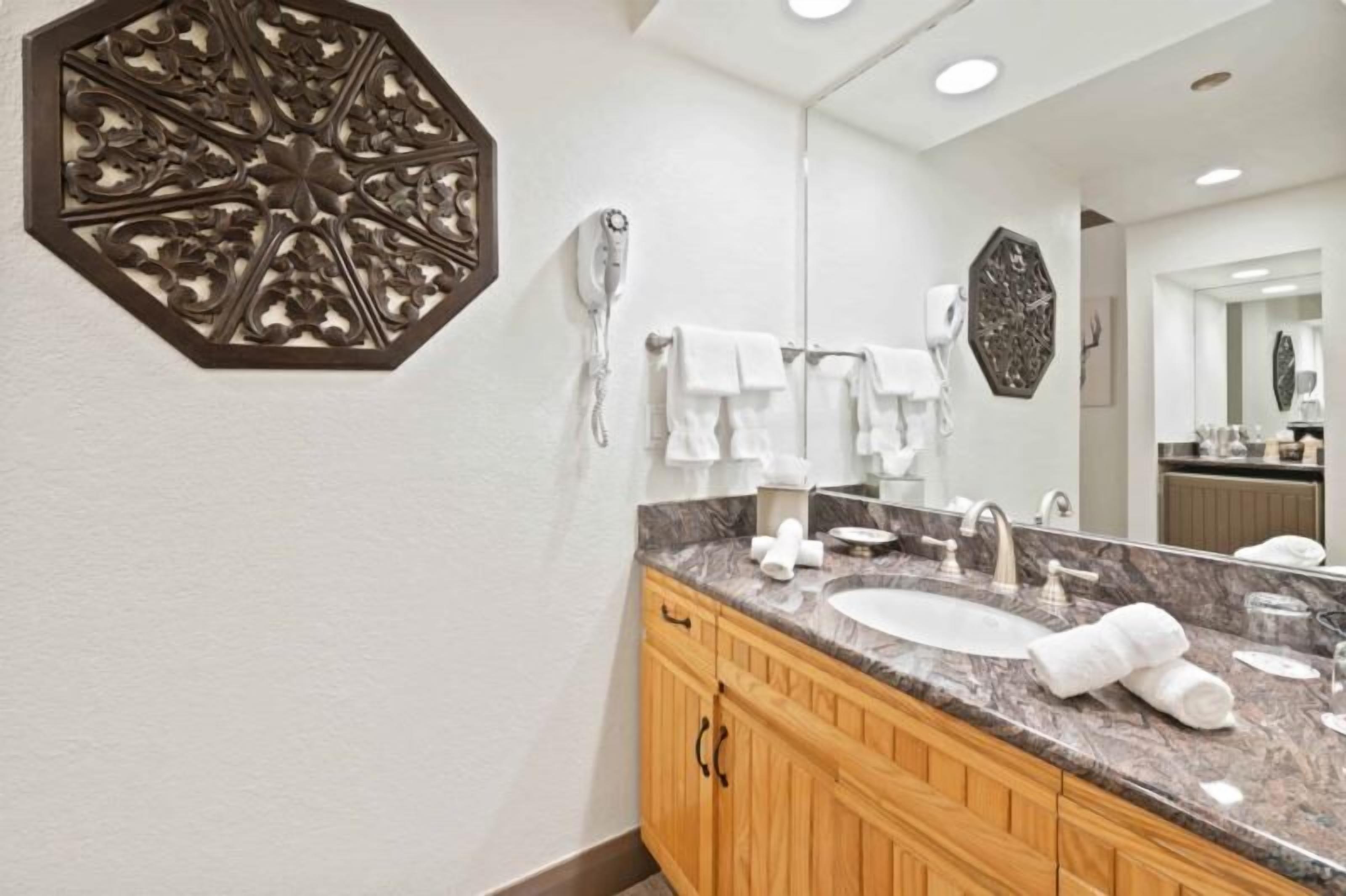 A modern bathroom with a marble sink, wooden cabinets, a large mirror, and decorative wall art.
