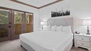 Ein Schlafzimmer mit einem großen Bett, einem Nachttisch mit Lampe, einem Wandbild und einer Tür mit Glasfenster.