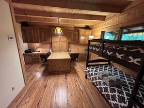 A cozy cabin interior with wooden floors, a bunk bed, a kitchen area with wooden cabinets, and a hanging light fixture. - Luxury lodge in the heart of the Bluegrass (Waddy)