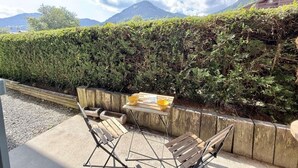 Un espace extérieur aménagé avec une table et des chaises, un banc en bois et une vue sur une chaîne de montagnes.