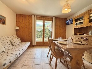 A cozy room with a wooden sofa, a dining table with chairs, and a view through a glass door. - Ground floor, terrace, parking, tv, ski locker, 19m², Praz sur Arly (Praz-sur-Arly)