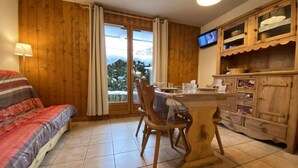 Une pièce confortable avec un lit, une table à manger et des chaises, un meuble en bois et un téléviseur fixé au mur.