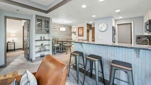 A modern kitchen with a bar area, built-in shelves, and a dining area with chairs.