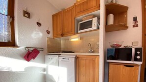 A compact kitchen with wooden cabinets, a microwave, a dishwasher, and a small sink. - 1st floor, balcony, parking, tv, ski locker, 25m², Praz sur Arly (Praz-sur-Arly)
