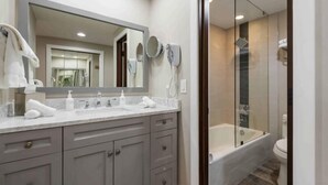 Une salle de bain moderne avec un grand miroir, deux lavabos, une baignoire et une douche séparée par une paroi en verre.