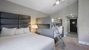 Une chambre à coucher avec un grand lit, une table de chevet, un bureau, une chaise, une échelle et un ventilateur de plafond.