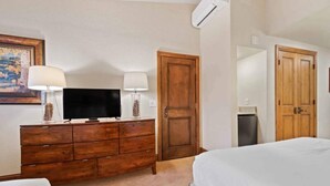 Ein Hotelzimmer mit einem hölzernen Schminktisch, einem Fernseher, zwei Lampen, einem Bett und einer Tür.