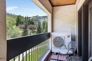 A balcony with a Mitsubishi Electric air conditioner, a chair, and a view of a forested area.