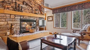 Un salon chaleureux avec une cheminée en pierre, des fauteuils confortables et une grande fenêtre donnant sur la forêt.