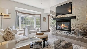 A modern living room with a fireplace, a large window, and a flat-screen TV mounted above it.