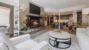 A modern living room with a fireplace, a dining area, and a kitchen in the background.