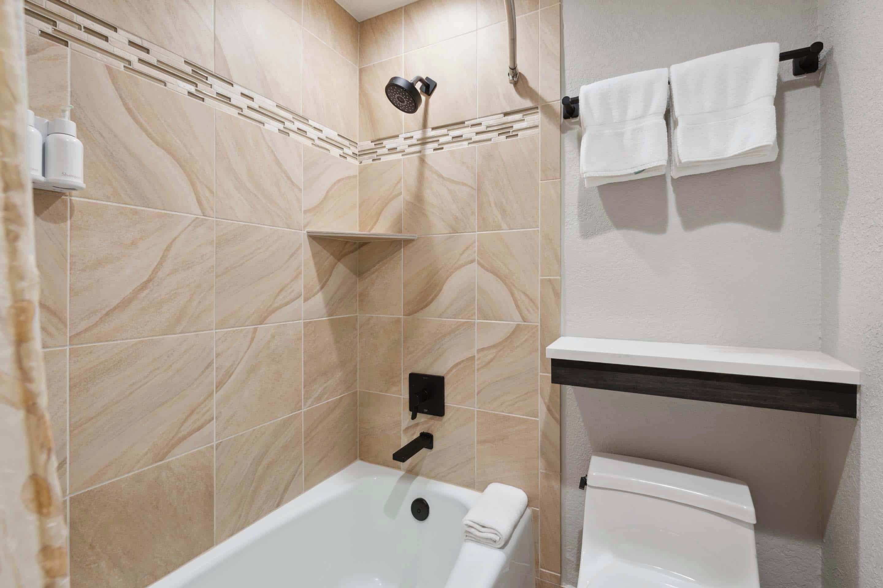 A bathroom with a bathtub, a showerhead, a toilet, and a towel rack with towels.